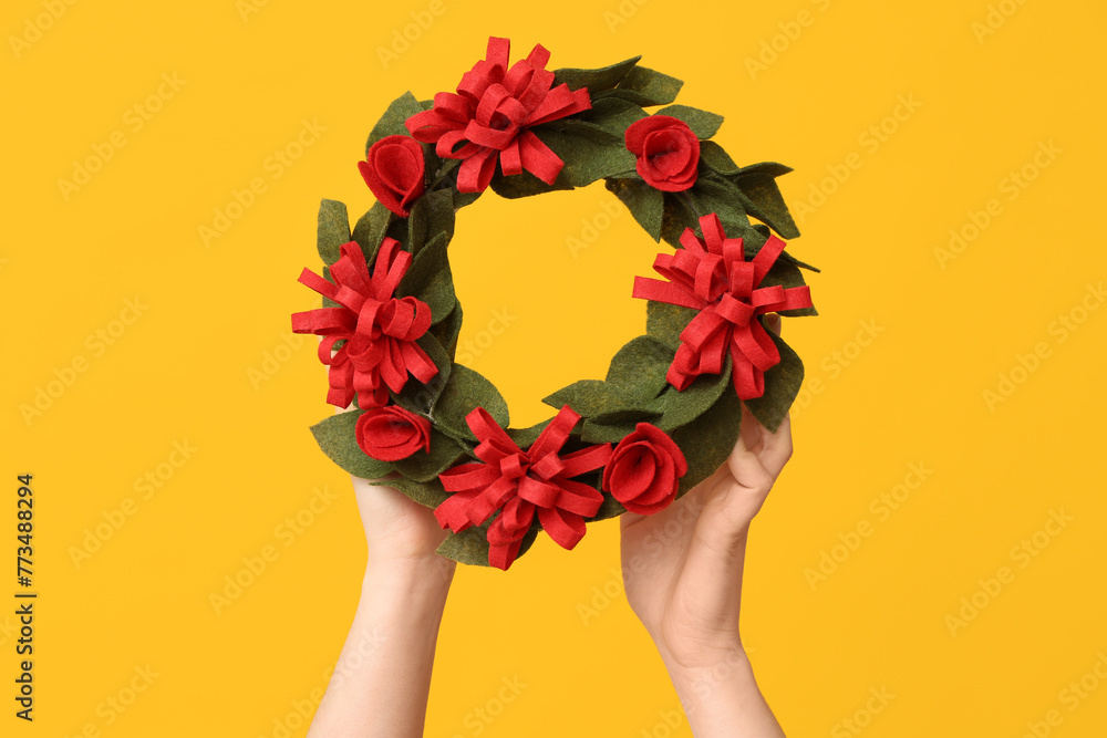 Female hands with Easter festive wreath on yellow background