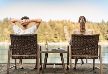 Young couple on holiday vacation relaxing drinking wine reading and enjoying beautiful nature lake setting 