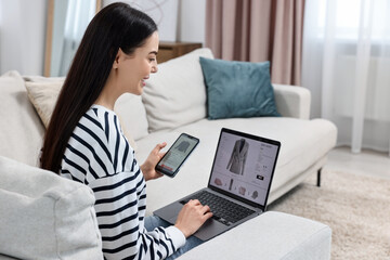 Wall Mural - Beautiful young woman with smartphone and laptop shopping online at home