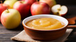 Apple sauce in a bowl under bright daylight with whole and halved fruits nearby; background image
