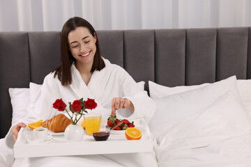 Wall Mural - Smiling woman having breakfast in bed at home, space for text