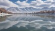 In the winter, there is heavy snow on both sides of West Lake in China's Gansu Province with snowy mountains and a cloudy sky in the distance. The lake water reflects white clouds like mirror reflecti