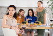 Woman looking hurt and upset during argument with female friends sitting at table in background showing disapproval and discontent during home party..