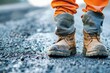 Close up of a civil engineer's boots standing firm on freshly laid asphalt of a new highway, marking progress.