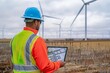 A civil engineer at a wind farm construction site, analyzing turbine placement with a digital tablet.