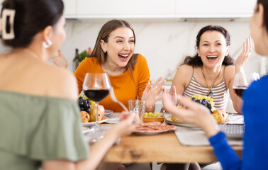 Wall Mural - Group of women friends talking and drinking wine at party in kitchen