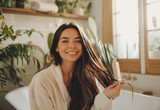 Fototapeta Panele - Happy woman in bathrobe sitting on edge of bathtub, using hair brush to clean long straight dark brown hair and smiling at camera