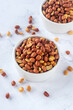Roasted salted peanuts in white ceramic bowl on white marble background.