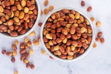 Wall Mural - Roasted salted peanuts in white ceramic bowl on white marble background.