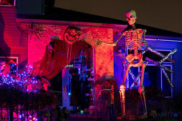 Wall Mural - Illuminated night Halloween house outdoor decorations with skeleton and monsters near the house in red and purple light