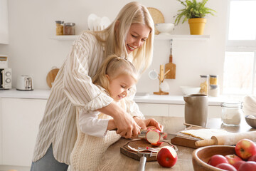 Poster - Young woman with her little daughter cutting apple for pie in kitchen