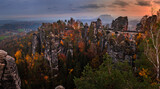 Fototapeta Big Ben - Saxon, Germany - Panoramic view of the Bastei bridge with a sunny autumn sunset with colorful foliage and sky. Bastei is famous for the beautiful rock formation in Saxon Switzerland National Park