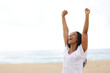 Happy black woman raising arms celebrating on the beach