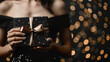 Beautiful young woman in a black dress with a gift box in her hands on a dark background and golden bokeh