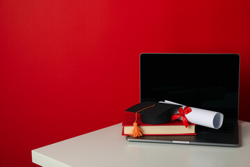 Wall Mural - Graduate hat with diploma, book and laptop on red background.