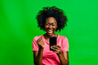Exuberant woman with afro hair celebrating a victory or good news on her smartphone against a green background