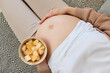 Wellness in pregnancy eating. Leisurely maternity meal. Love for healthy eating. Top view of unknown pregnant woman with bare belly holding bowl with fruits and touching her tummy