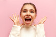 shocked teenage girl with braces screams with raised hands in fear on pink isolated background, surprised child with mouth open in amazement