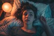 Restless young woman in bed with a concerned look, room bathed in lamp light