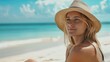 Pretty blond woman in straw hat sitting on tropical beach, enjoying holidays near ocean.
