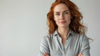 Confident young woman with red hair and freckles standing against a neutral background, arms crossed, wearing a casual gray shirt, looking directly at the camera with a soft smile.