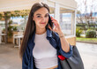 Cheerful pretty young woman talking on phone and look at camera. Holding smartphone close to ear. Standing alone outside