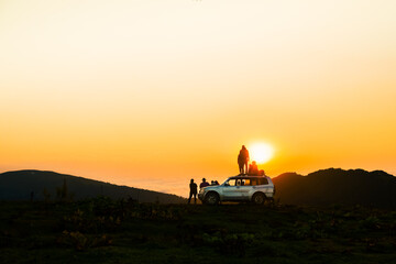 akhmaro, Georgia - 14th august, 2022: Static view friends tour group stand on 4wd rooftop watch sunset together outdoors have fun above clouds in famous travel destination