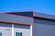 Industrial office building next to metal warehouse against blue clear sky background, side view with copy space