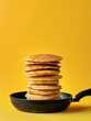 A towering pile of fresh pancakes drizzled with sticky syrup captured just as droplets begin to fall, set against a vivid yellow background.