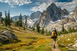 A man steadily hikes up a trail in the mountains, surrounded by towering peaks and vast wilderness