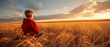   A young boy, clad in a red jacket, stands in a field of golden wheat, gazing into the distance The sun sets behind him, painting the sky with warm hues