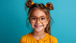 © amixstudio - Portrait of a smiling young girl with glasses and double buns hairstyle on a blue background.