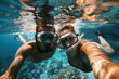 A man and woman are underwater, wearing scuba gear and taking a selfie