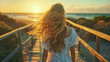 Woman walking in beach at sunset, Back view portrait of young girl walking on wooden boardwalk in evening, hair blowing with wind and glowing with sun light