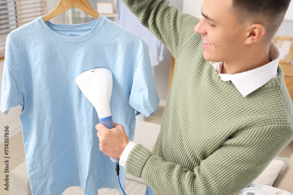 Happy young man steaming blue t-shirt at home