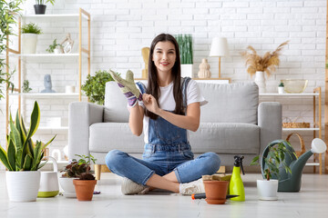 Sticker - Beautiful young female gardener with houseplants wearing gardening gloves at home