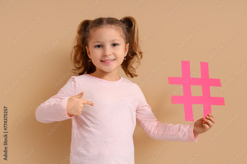 Cute little girl pointing at hashtag on beige background