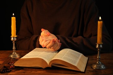 Woman praying at table with burning candles and Bible, closeup