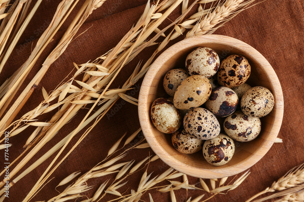 Wooden bowl with fresh quail eggs and wheat on napkin
