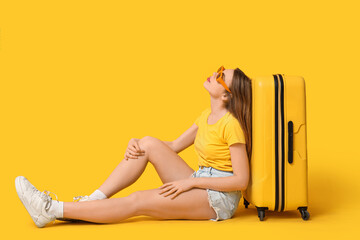 Sticker - Beautiful young woman with yellow suitcase sitting against color background