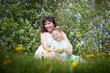 Happy mother and daughter enjoying rest, playing and fun on nature on a green lawn with dandelions and blooming apple tree on the background. Woman and girl resting outdoors in summer and spring day