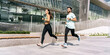In this lively scene, a pair of runners exude the essence of vitality and companionship as they jog in unison along an urban path, enveloped by the day's clear skies.