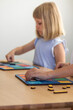 © Виктория Попова - A cute girl is playing a logical wooden game at a table in a room. Children's wooden educational toy