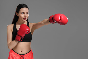 Poster - Beautiful woman in boxing gloves training on grey background. Space for text