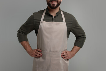 Canvas Print - Smiling man in kitchen apron on grey background, closeup. Mockup for design