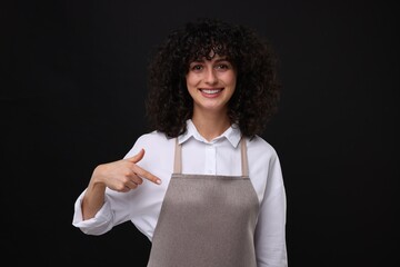 Wall Mural - Happy woman pointing at kitchen apron on black background. Mockup for design