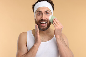 Wall Mural - Man with headband washing his face using sponge on beige background