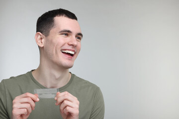 Wall Mural - Young man with whitening strips on light grey background. Space for text