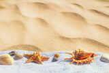 Fototapeta Na ścianę - View of a beach sand with towel and seashells under the hot summer sun, selective focus. Concept of sandy beach holiday, background with copy space for text