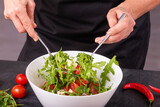 Fototapeta Na ścianę - The cook mixes fresh vegetable salad with mozzarella cheese in a bowl, closeup with selective focus